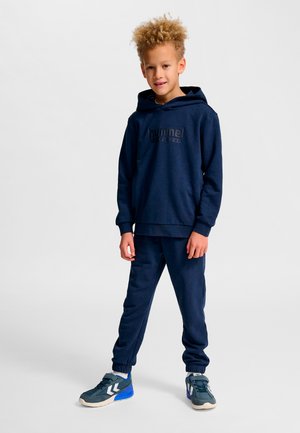 Marineblauer Kapuzenpullover und passende Jogginghose aus weichem Stoff, mit Kängurutasche und einem Logo vorne. Sportschuhe in Grau und Blau.