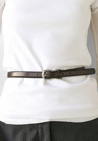 Talje med hvid skjorte stoppet ned i mørke bukser med tynde striber, holdt på plads af et mørkebrunt læderbælte med spænde i sølv.