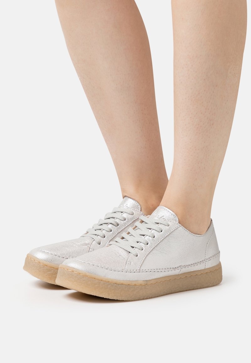 Baskets argentées métalliques avec bout rond, design à lacets, empeigne texturée et semelle en caoutchouc beige clair. Finition lisse avec des détails subtils.
