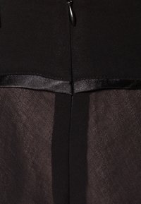 Gros plan d'une fermeture éclair noire sur un vêtement avec un bord satiné le long de la couture sur un tissu texturé.