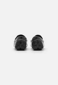 Chaussures noires avec une surface texturée et des talons arrondis. Présentent un design bas, des semelles en caoutchouc avec des motifs de traction et un design à enfiler.