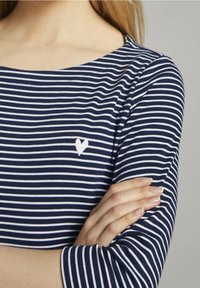 Niebiesko-białe pasiastą bluzkę z długim rękawem, z dekoltem łódka i małym białym haftem serca na piersi, wykonaną z miękkiego materiału.