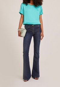 Turkos satinblus med uppvikt ärm, kombinerad med mörkblå utsvängda jeans och en liten mintgrön handväska. Släta texturer och avslappnad passform.