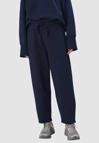Marineblauwe joggingbroek met een taillekoord, voorzien van een losse pasvorm en een zachte stoftextuur. Gecombineerd met grijze sportieve sneakers.