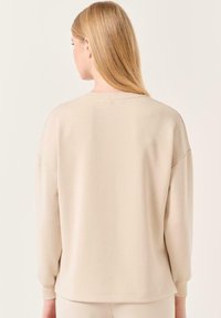 Felpa oversize beige con polsini e scollatura a coste, caratterizzata da una texture liscia e una vestibilità comoda. Mostrata da dietro.