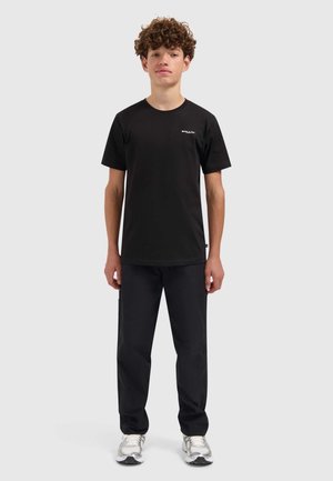 Zwart T-shirt met korte mouwen en ronde hals, met een wit logo op de linkerborst, gecombineerd met zwarte broek en zilveren sneakers.