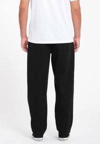 Zwarte katoenen broek met een relaxte pasvorm, rechte benen en een elastische tailleband, gecombineerd met witte sneakers met een logo.