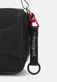 Borsa nera in tessuto con motivi embossati, dotata di una clip argentata e di un moschettone rosso. Include una tracolla in pelle con logo.