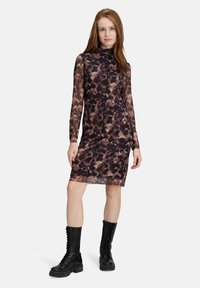 Durchsichtiges langärmliges Kleid mit einem braun-schwarzen Leopardenmuster, das einen hohen Kragen und eine taillierte Silhouette aufweist. Kombiniert mit schwarzen Combat-Stiefeln.