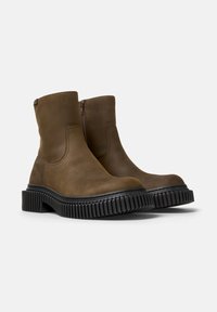 Botas de tobillo marrones con una suela negra texturizada y un cierre lateral, exhibidas sobre un fondo blanco liso.