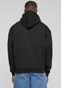Black hooded sweatshirt with a relaxed fit, ribbed cuffs and hem, made from soft fabric, viewed from the back with mid-blue jeans.