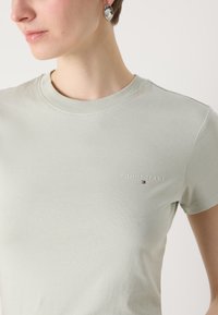 Ljusgrön bomullströja med rund halsringning och litet broderat "TOMMY JEANS"-logotyp på bröstet. Slät textur, åtsittande design.