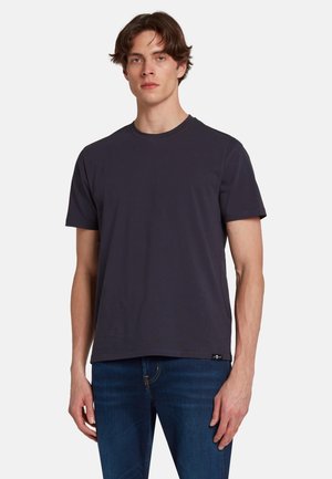 Maglietta in cotone grigio scuro con maniche corte, scollatura rotonda e un piccolo etichetta del logo sull'orlo; indossata con jeans blu.
