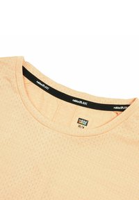 Camisa de color durazno, de manga corta, con una tela texturizada y un escote redondo. Presenta una etiqueta negra con un logotipo blanco en el interior del cuello.