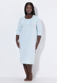Světle modrá noční košile z měkké látky, s 3/4 rukávy, zapínáním na knoflíky a krajkovou ozdobou podél lemu. Celkově hladká textura.