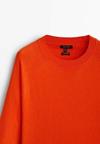 Pull col rond orange vif avec col côtelé et étiquette de marque visible à l'intérieur de l'encolure, posé à plat sur fond blanc.