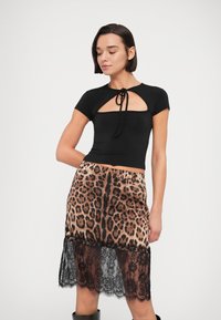 Μαύρο κοντό τοπ με σχέδιο κλειδαρότρυπας και λεπτομέρεια δέσιμου, συνδυασμένο με φούστα λεοπάρ με μαύρη δαντέλα στο τελείωμα.