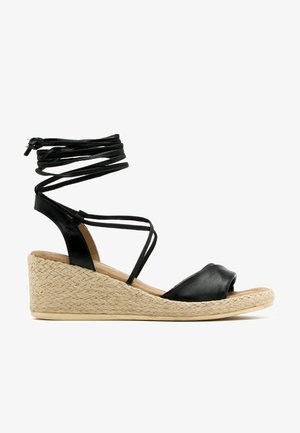 Sandalia de cuña de cuero negro con suela de yute trenzado y tiras alrededor del tobillo, punta descubierta y tacón bajo, adecuada para el uso casual.