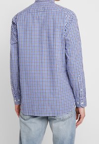 Camicia a maniche lunghe a quadri blu e bianchi con colletto bottonato, caratterizzata da un orlo curvo e polsini bottonati. Tessuto in cotone con una texture liscia.