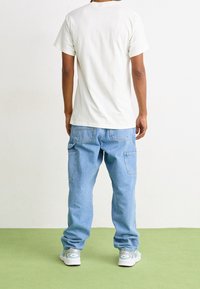 Camiseta de algodón blanca de manga corta, combinada con pantalones vaqueros baggy de mezclilla azul claro con bolsillos laterales, y zapatillas de color claro.