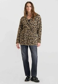 Leopardprint cardigan in beige en zwart, gemaakt van een gestructureerde gebreide stof, met een tailleceintuur, gecombineerd met donkere denim jeans en zwarte schoenen.
