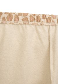 Beige weicher Stoff mit einem elastischen Bund im Leopardenmuster. Die Textur wirkt glatt und weist feine Nähte entlang der Kanten auf.