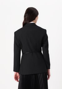 Black tailored blazer with a fitted silhouette, long sleeves, and a cinched waist. Smooth fabric, detailed stitching, and no visible patterns.