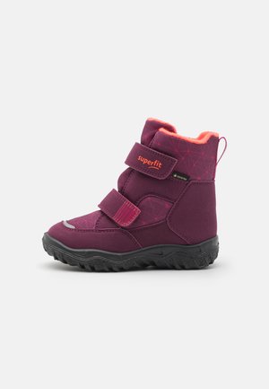 Lila Winterstiefel mit Klettverschlüssen, isolierter Innenauskleidung, strukturiertem Obermaterial, Gummisohle und orangefarbenen Akzenten. Geeignet für kaltes Wetter.