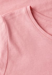 Nahaufnahme eines hellrosa Baumwoll-T-Shirts mit rundem Ausschnitt und glatter Textur. Nähte sind am Kragenrand sichtbar.