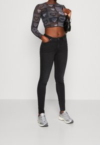 Svarta tajta jeans i kombination med en genomskinlig långärmad topp med hjärtmönster. Accentuerat med en svart handväska och silvriga sneakers.