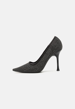 Black high-heeled pump with pointed toe, embellished with small silver studs, featuring a textured upper and sleek stiletto heel.