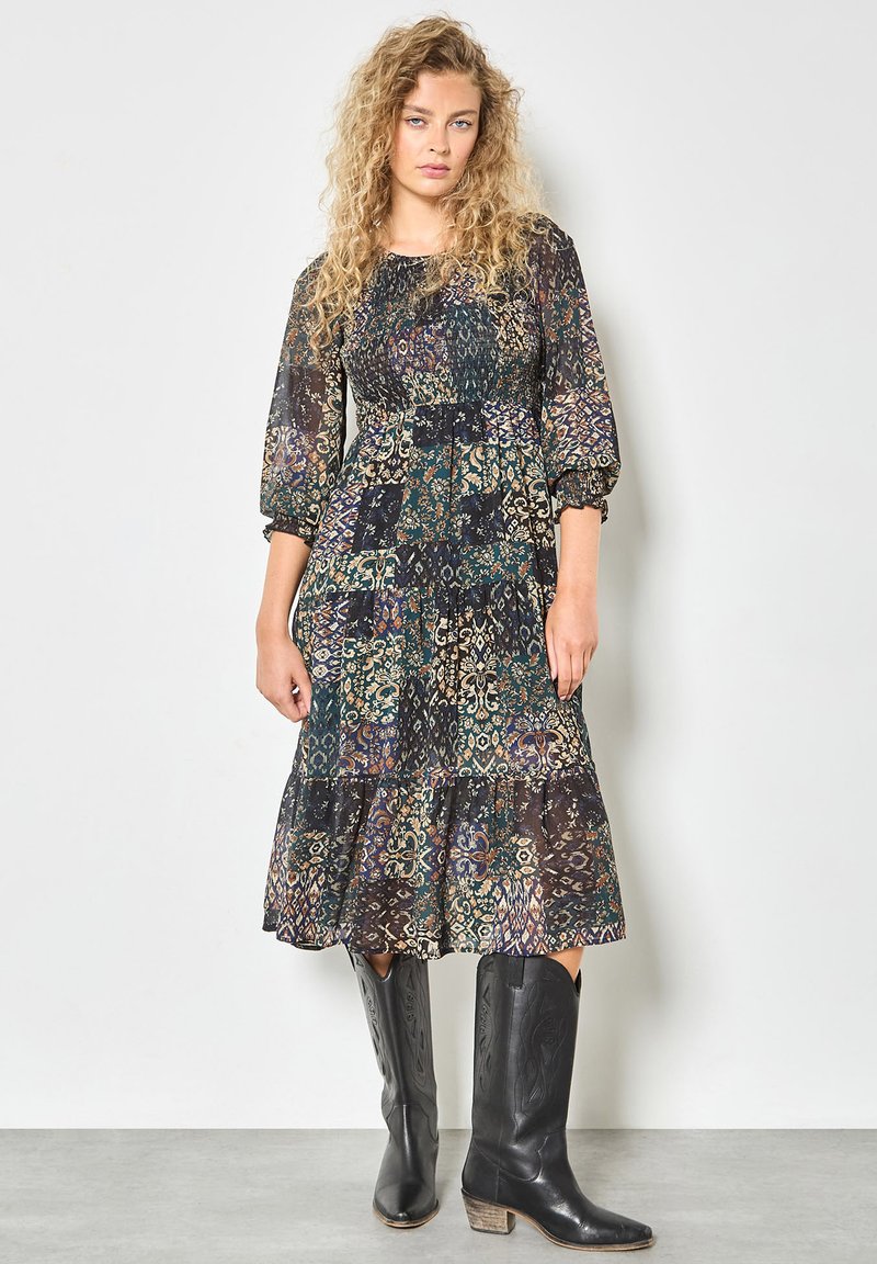 Abito nero floreale con maniche lunghe a palloncino, gonna a strati e motivi multicolori. Indossato con stivali da cowboy neri.