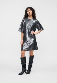 Φόρεμα με κοντά μανίκια καλυμμένο με ασημένιες παγιέτες, ελαφρώς σε σχήμα Α, μέχρι το γόνατο, συνδυασμένο με μαύρες μπότες με τακούνι μέχρι το γόνατο.