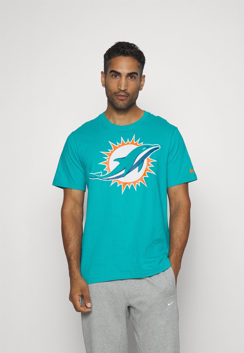Türkisfarbiges Baumwoll-T-Shirt mit Miami Dolphins-Logo, orangefarbenem Sonnenstrahlen-Design und kurzen Ärmeln. Kombiniert mit grauen Sweatpants, die eine lockere Passform zeigen.