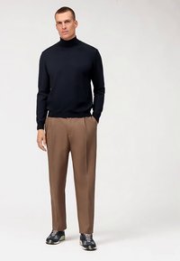 Marineblauer Rollkragenpullover, braune Hose und schwarze Sneakers. Weicher, glatter Stoff; tailliertes Design; neutrale Farbpalette; legerer Look.