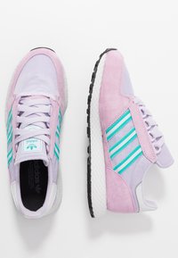 Des chaussures de sport violettes et roses en mesh et en suède, avec des rayures turquoise et une semelle intermédiaire blanche texturée, conçues pour le confort.