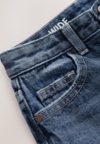 Nahaufnahme des Taillenbunds und der Vordertasche aus blauem Denim mit sichtbarer Gürtelschlaufe und Metallniete.