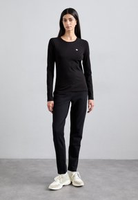Svart langermet skjorte med rund hals og liten logo, kombinert med svarte slim-fit bukser og lyse sneakers.