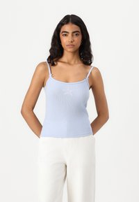 Light blue ribbed tank top with thin straps, featuring a front star design and decorative ties at the straps. Paired with white pants.