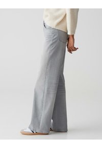 Lichtgrijze wijde jeans met een gladde textuur, voorzien van een klassieke vijf-pocketontwerp en een licht vervaagd uiterlijk, gecombineerd met witte sneakers.
