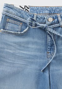 Lichtblauwe denim jeans met een strikceintuur, voorzakken en een verwerkte rand. Voorzien van een zilveren metalen knoop en stikselaccenten.