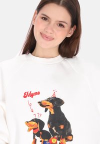 Weißes Sweatshirt mit einem bunten Motiv von zwei Dackeln, von denen einer einen Partyhut trägt, und dem roten Schriftzug "Mymo" darüber.