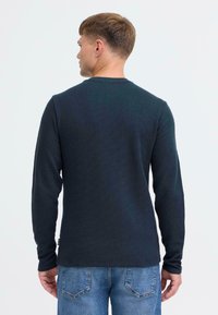Maglia termica a maniche lunghe di un blu navy scuro con un motivo testurizzato, scollatura rotonda e orlo dritto, abbinata a jeans azzurri chiari.