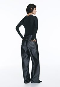 Čierne tričko s dlhými rukávmi a textúrovaným zadným dielom, kombinované s voľnými tmavými džínsami s klasickým vreckovým dizajnom a jemným leskom.