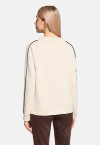 Bluza w kolorze kremowym z czarnymi paskami po bokach, luźny krój, ściągacze na mankietach i u dołu. Gładka tekstura, prosty design, bez widocznych logo czy wzorów.