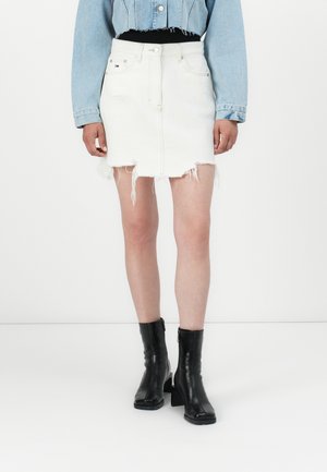 White denim skirt with frayed hem, front pockets, and zip fly. Paired with a black top and black heeled ankle boots.