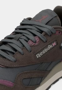 Close-up de um ténis Reebok cinza e castanho com atacadores grossos, materiais de camurça e malha, e o logótipo da União Jack na lateral.