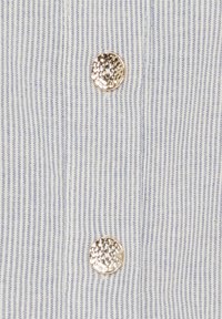 Blå og hvid stribet stof med to dekorative guldknapper, der har en struktureret overflade, der fremhæver lodrette linjer og en blød tekstur.