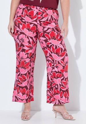 Spodnie z szerokimi nogawkami z dużym czerwono-różowym kwiatowym nadrukiem, noszone z beżowymi sandałami na obcasie z paskami na białym tle.