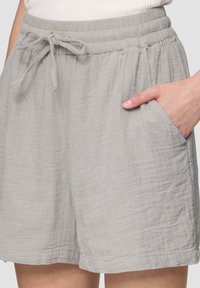 Shorts gris clair en tissu texturé, dotés d'une taille élastique avec cordon de serrage et de poches latérales. Design simple et décontracté.